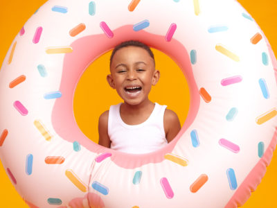 Enjoyment, fun, joy and happiness concept. Cheerful overjoyed dark skinned little boy feeling excited, going to beach with his father, laughing out loud, posing in studio with inflatable circle